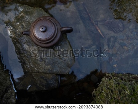 Clay teapot standing on the stone. By the river. Transparent flow. Reflections and glare in the water. Beauty of nature.