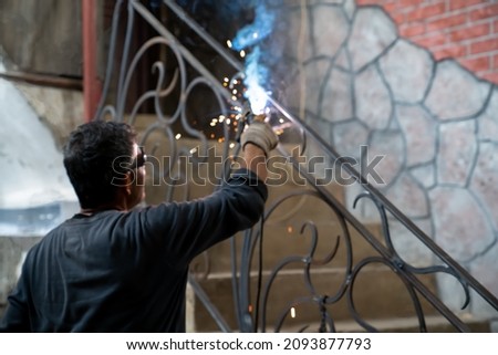 Man in safety glasses is welding metal of staircase. Welding work on metal in private house. blurred background.