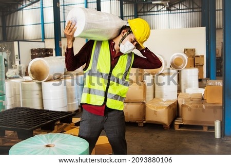 
Male workers carry heavy rolls of fabric over their shoulders to move them into production and are at risk of injury from lifting too heavy loads many times without weight-lifting equipment. Royalty-Free Stock Photo #2093880106
