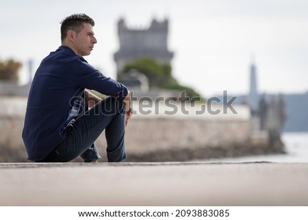 Portrait of a young classy entrepreneur relaxing alone along the Lisbon riverside in Portugal. Classy business man wearing a blue elegant shirt and formal outfit. Successful lifestyle concept. Royalty-Free Stock Photo #2093883085