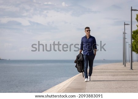 Portrait of a young classy entrepreneur relaxing alone along the Lisbon riverside in Portugal. Classy business man wearing a blue elegant shirt and formal outfit. Successful lifestyle concept. Royalty-Free Stock Photo #2093883091