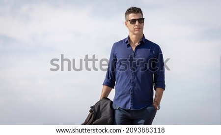 Portrait of a young classy entrepreneur relaxing alone along the Lisbon riverside in Portugal. Classy business man wearing a blue elegant shirt and formal outfit. Successful lifestyle concept. Royalty-Free Stock Photo #2093883118