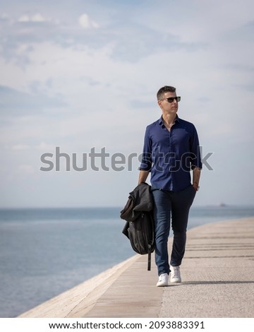 Portrait of a young classy entrepreneur relaxing alone along the Lisbon riverside in Portugal. Classy business man wearing a blue elegant shirt and formal outfit. Successful lifestyle concept. Royalty-Free Stock Photo #2093883391