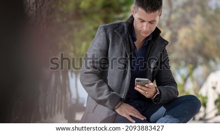 Classy freelance architect sitting alone on a bench outdoor and talking on the phone during a beautiful summer day. Classy small entrepreneur using the smart phone along the riverside in Lisbon Royalty-Free Stock Photo #2093883427