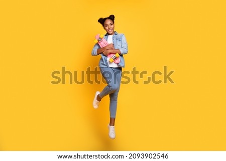 Full length photo of young african girl jump up energetic hug skateboard weekend isolated over yellow color background