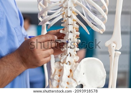 Close up of nurse pointing at spine bones on human skeleton to explain diagnosis to senior patient. Assistant showing spinal cord to old man for physical recovery and chiropractic remedy Royalty-Free Stock Photo #2093918578