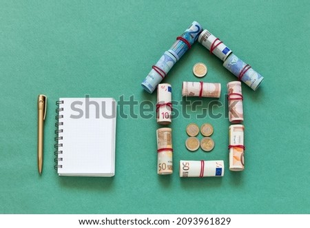 Family budget planning concept. Money to buy a home. Loan for building a house. Symbolic house made of twisted euro banknotes and a notebook with a pen on a green background