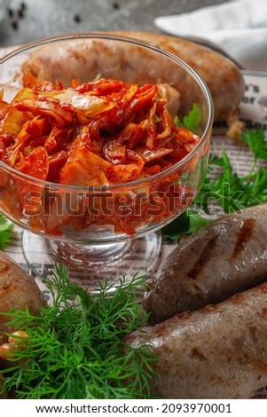 Serving a dish from a restaurant menu. Grilled kupats, Georgian sausages with cilantro and parsley greens with pickled cabbage and spices on a plate against a gray stone table