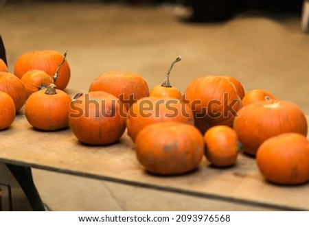 There are many pumpkins for sale on the table. A pumpkin is sold at a holiday to carve a face and light a candle