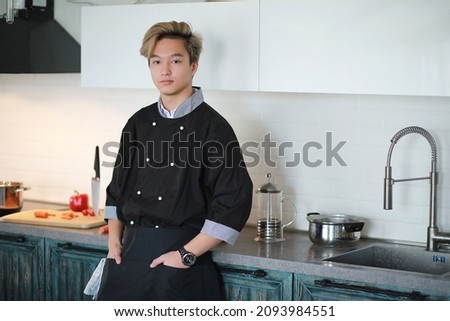A young Asian cook in the kitchen prepares food in a cook suit
