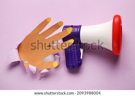 Toy megaphone and paper hand visible through torn color paper