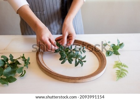 Woman puts branches of plants into frame for making botanical bas-relief. Female hands for working with clay, plasticine on desktop, top view. High quality photo