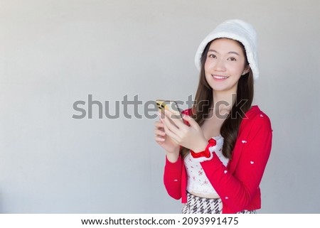 Portrait of a pretty Asian woman wearing a red dress and white hat happily using a smartphone on a white background.