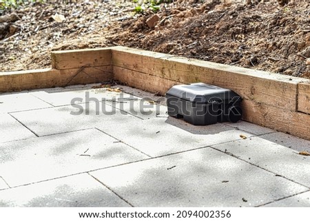 Black rodent bait and trap station being used outside a building to control rats.  Royalty-Free Stock Photo #2094002356