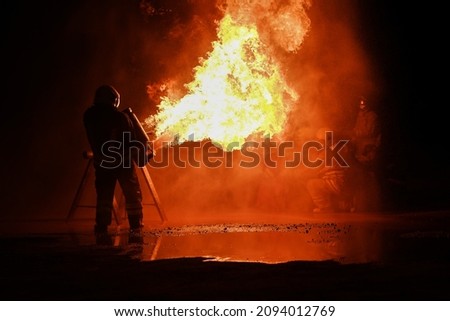 Firefighters wear fire protective clothing to spray fire from tanks for nighttime fire drills.