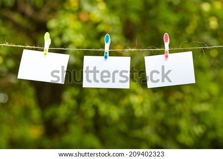 Blank pieces of paper hang on clothesline on green garden  background 