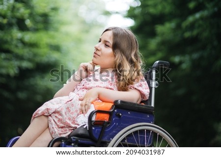 Female person with spinal muscular atrophy spending time outdoors alone with her thoughts. Young woman who using wheelchair sitting among green summer park and looking aside. Royalty-Free Stock Photo #2094031987