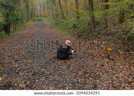 A photographer girl taking nature in autumn. She has brown hat. Leaves on ground. Hobby concept. Unrecognizable person.
