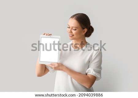Beautiful young woman holding tablet computer with blank screen on grey background