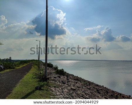 Stock photo of clean and empty asphalt next to bennithora dam, solar electric pole installed nearby road, blue sky with white clouds on background. Picture captured under bright sunlight at herur.