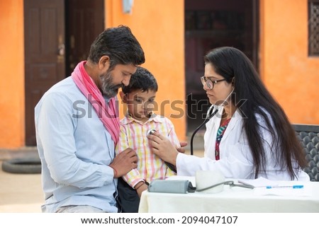 Indian female doctor with stethoscope checking little child patient heart beat or breath at village, Kid with his father getting examine by medical person, Rural India healthcare concept Royalty-Free Stock Photo #2094047107