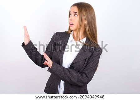 Displeased Young business woman wearing jacket over white background keeps hands towards empty space and asks not come closer sees something unpleasant