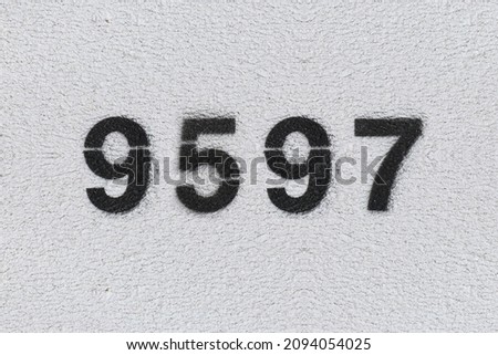 Black Number 9597 on the white wall. Spray paint. Number nine thousand five hundred ninety seven.