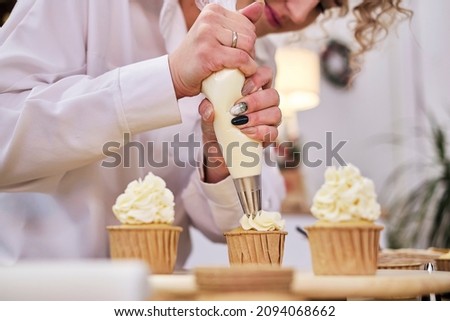 Pastry bag with white cream. Making homemade cupcakes with a pastry bag. process of decorating cupcakes with white whipped cream. Decorating a white cake with cream from the pastry bag. Royalty-Free Stock Photo #2094068662
