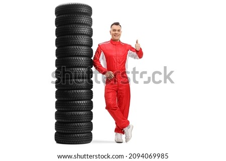 Full length portrait of a racer leaning on a pile of tires and gesturing a thumb up sign isolated on white background Royalty-Free Stock Photo #2094069985