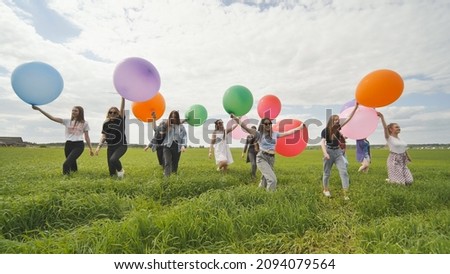 Girls friends are walking across the field with large balloons and colorful balloons.