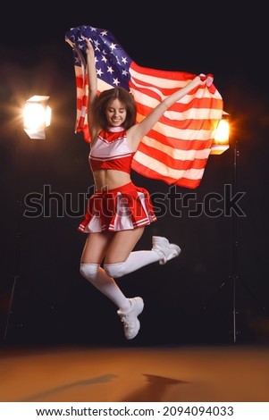 Beautiful young cheerleader with USA flag on dark background