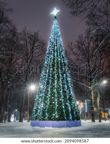 Artificial Christmas or New Year tree decorated with garlands in a winter night park with glowing lanterns.                   