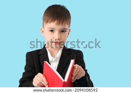 Little schoolboy reading book on color background