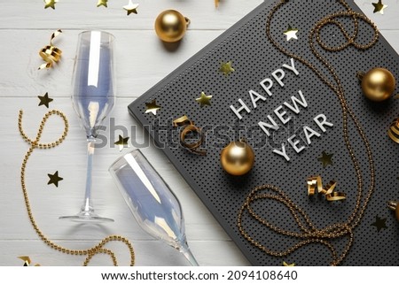 Board with text HAPPY NEW YEAR, glasses and Christmas decor on white wooden background
