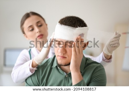 Doctor applying bandage onto head of young man in clinic Royalty-Free Stock Photo #2094108817