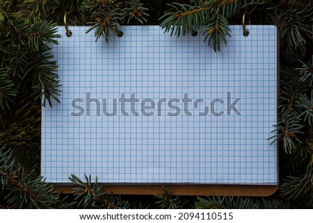 ring notebook with wood cover and blank checkered sheet on fresh spruce branches, mockup for the inscription on the theme of the new year