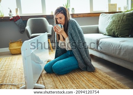 Woman in living room, focus on electric fan heater. Using heater at home in winter. Woman warming her hands. Heating season. Cold adult woman covered with clothes at home Royalty-Free Stock Photo #2094120754