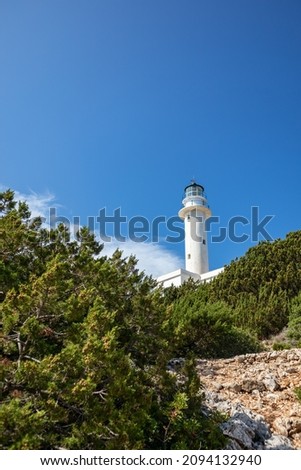 White lighthouse tall tower in pine greenery on clear blue sky in Greece, Ionian sea. Scenic travel destination. Lefkada island. Vertical
