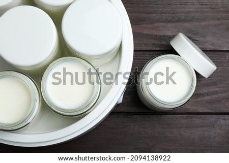 Modern yogurt maker with full jars on wooden table, flat lay