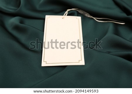 Blank white tag on green silky fabric, closeup. Space for text
