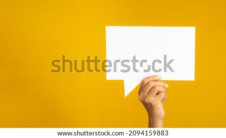 A speech bubble concept. Hand holding of an empty white speech balloon against a yellow background. Space for text. Close-up photo