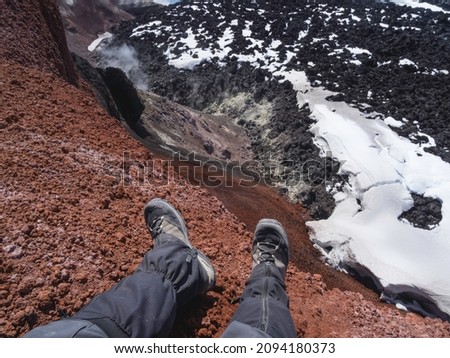 Top view on man's feet in hiking boots at caldera of Avachinsky stratovolcano, also known as Avacha Volcano. Backpacker tourist moves upon rocks behind steam from hot geysers. Kamchatka, Russia. Royalty-Free Stock Photo #2094180373