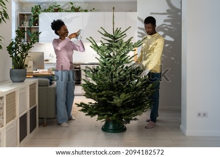 Young woman taking photo of fresh undecorated christmas tree for sharing in social media or blog. Happy couple busy install first xmas pine in new home prepare for new year winter holidays together