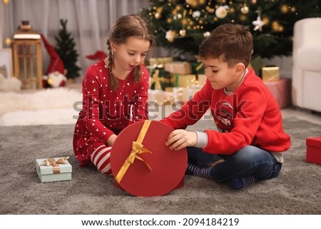 Cute little children opening gift box near Christmas tree at home