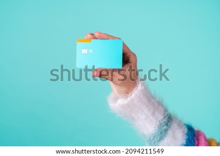 A girl's hand in a soft sweater holds a credit card on a turquoise background, empty space on a bank card for the inscription