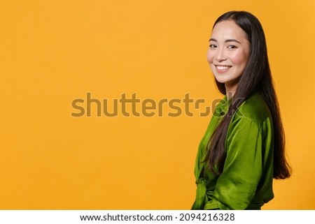 Side view of smiling charming pretty attractive beautiful young brunette asian woman 20s wearing basic green shirt standing looking camera isolated on bright yellow colour background, studio portrait Royalty-Free Stock Photo #2094216328