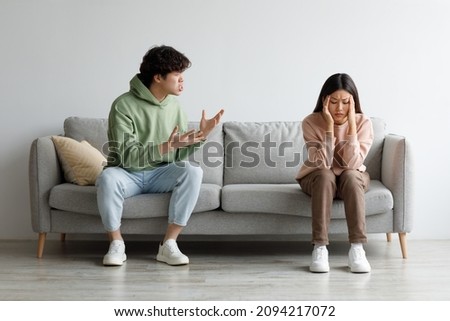 Misunderstanding in relationships. Millennial Asian couple quarrelling on couch at home, man shouting at his wife, copy space. Young spouses having conflict, arguing with each other indoors Royalty-Free Stock Photo #2094217072