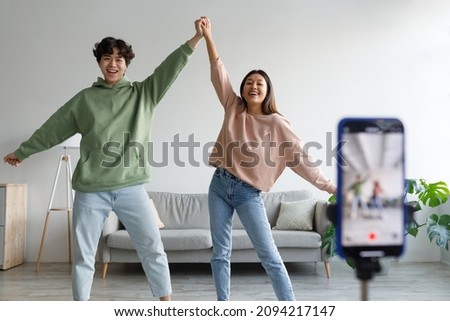 Happy young Asian couple making video on cellphone, dancing in front of camera at home. Lifestyle bloggers creating entertainment content for their vlog, live streaming together Royalty-Free Stock Photo #2094217147