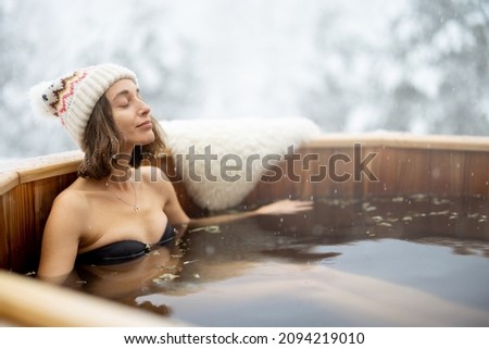 Woman relaxing in hot bath outdoors, enjoying thermal spa at snowy mountains. Winter holidays in the mountains, hot water treatments concept. Caucasian woman wearing winter hat Royalty-Free Stock Photo #2094219010