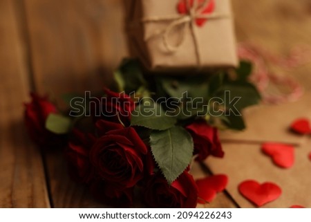 A bouquet of red roses on a wooden background, next to a letter with hearts and a gift. Picture for Valentine's Day. The concept of gifts and lovers. High-quality photography